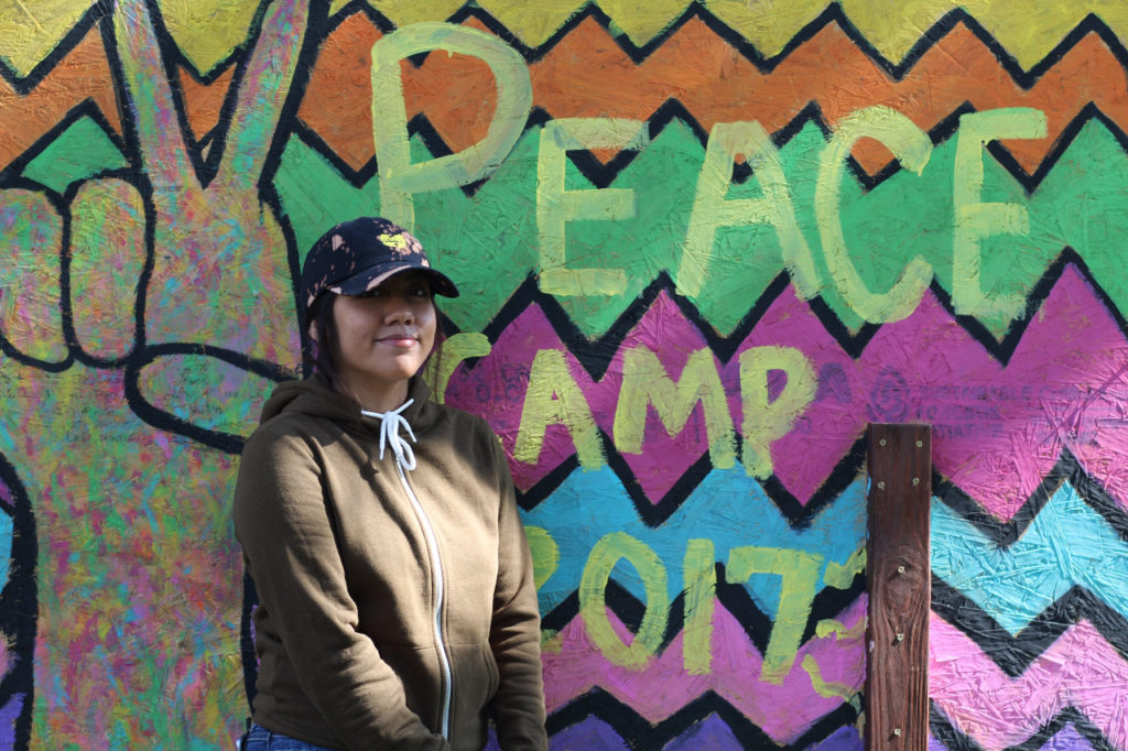 Sophomore Nadia Estrada poses in front of the Peace Camp signBYRON MASON II