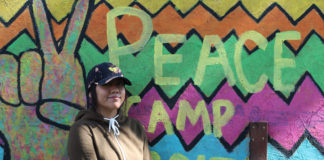Sophomore Nadia Estrada poses in front of the Peace Camp signBYRON MASON II